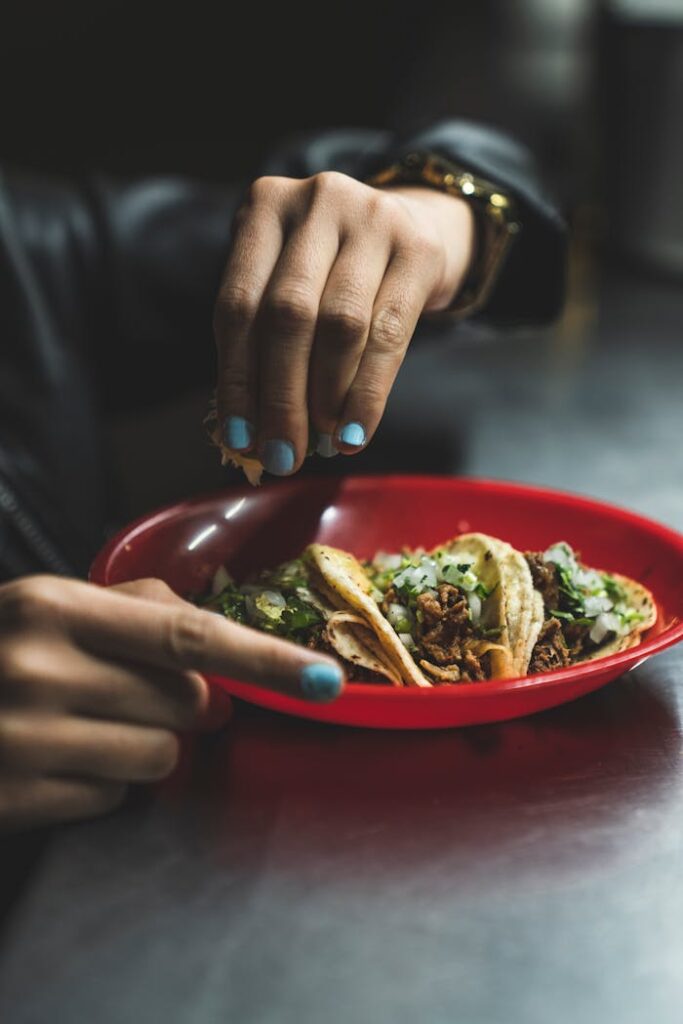 A Person's Hand Squeezing a Slice of Lime Over Tacos